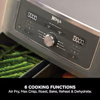 Close-up of a black and gray Ninja food processor control panel with digital displays and a dial, with green leafy vegetables visible in the bowl below.