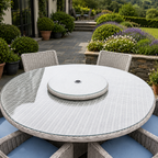 Round outdoor dining table set with a woven wicker-style frame, clear glass tabletop, matching chair backs, and a round center insert, shown in a landscaped patio garden.