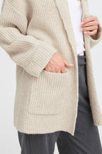 Person wearing a beige knitted cardigan on a white background