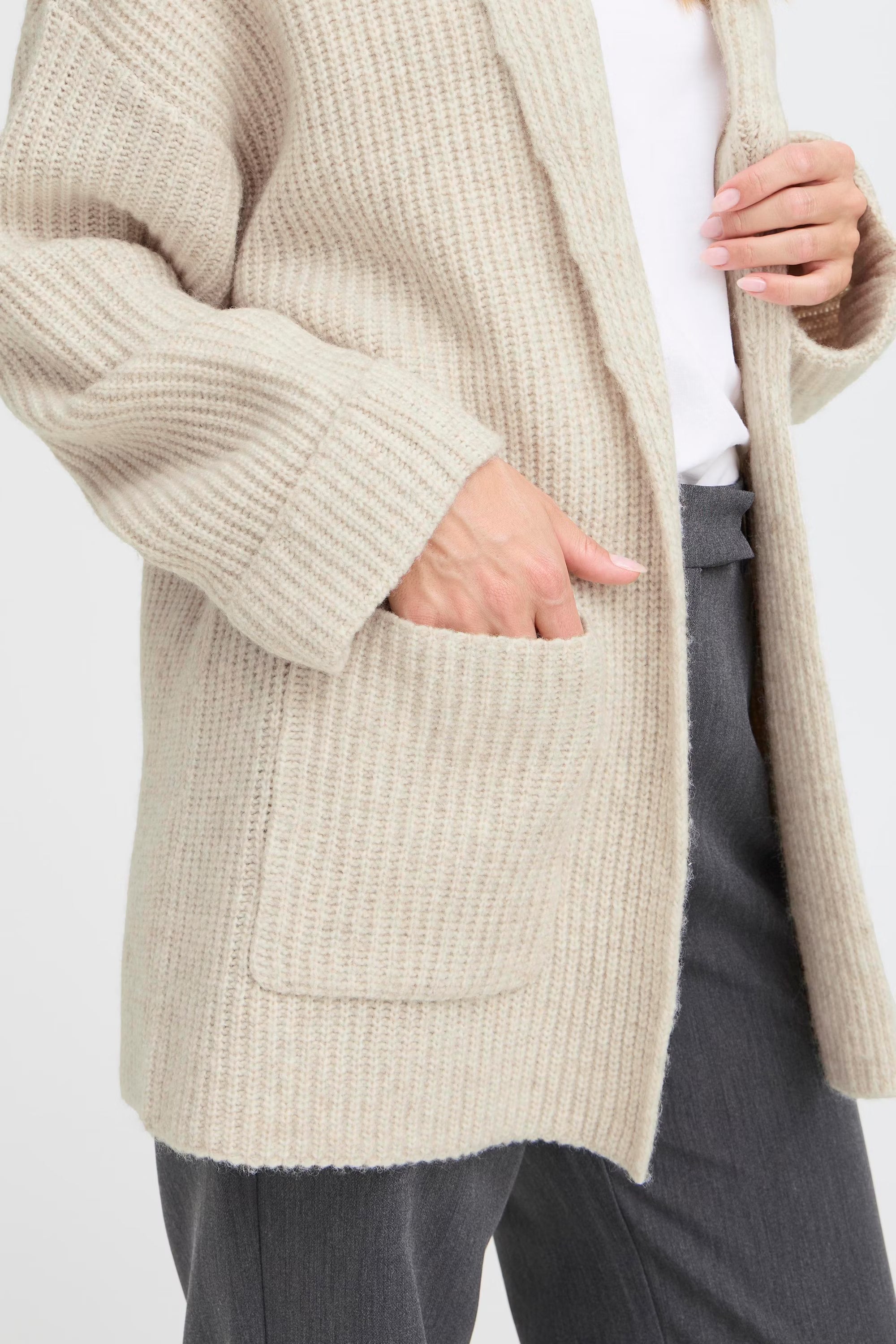 Person wearing a beige knitted cardigan on a white background