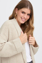 Woman wearing a beige cardigan over a white shirt on a light gray background