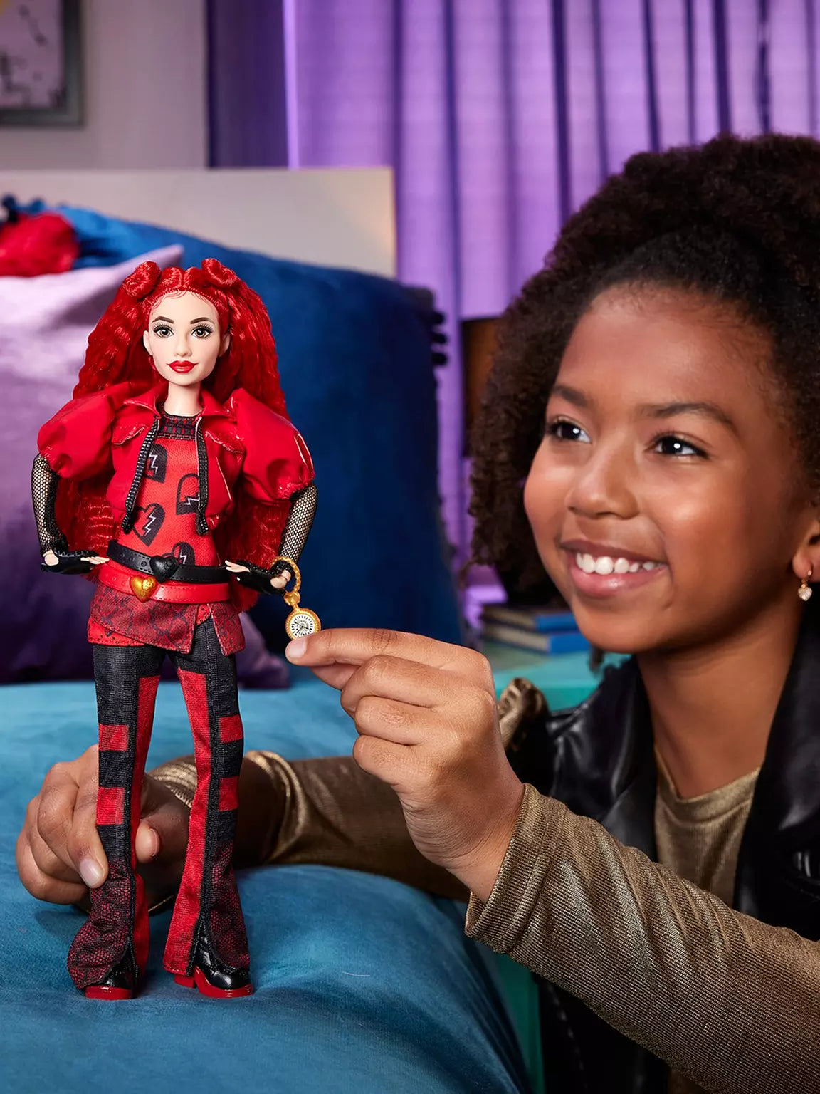 Child holding a Disney Descendants doll with red hair and red outfit, smiling.