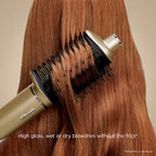 Hair dryer with brush attachment being used on long brown hair against a beige background