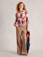 Woman wearing a colorful floral blouse and beige pants holding an umbrella on a plain background