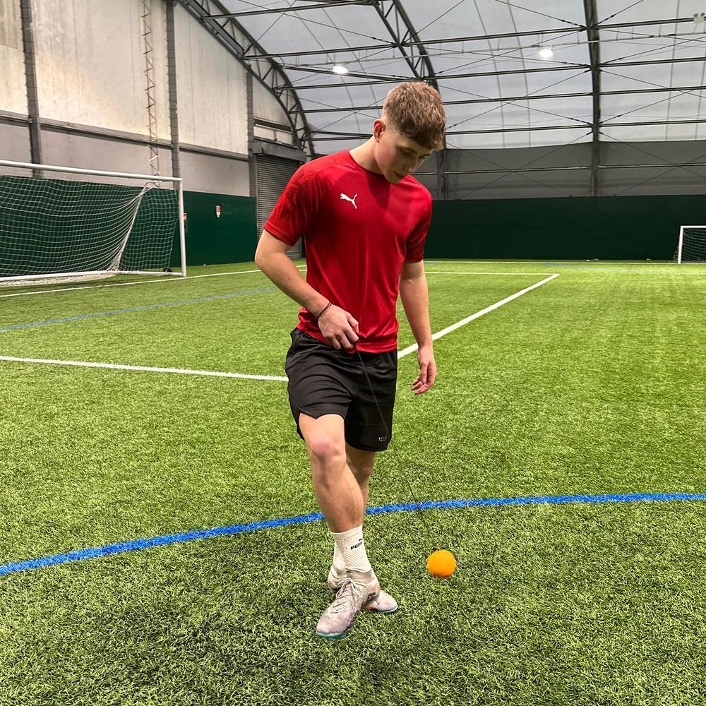 Person in a red shirt on an indoor sports field with a ball