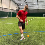 Person in a red shirt on an indoor sports field with a ball