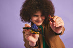 Person holding two small models against a purple background