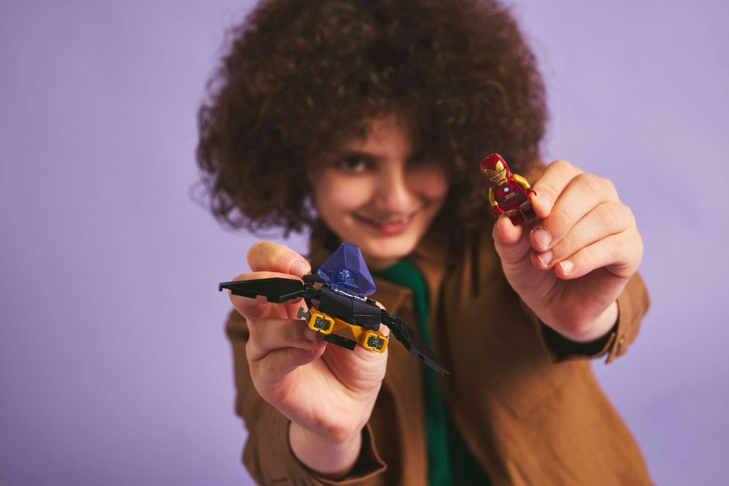 Person holding two small models against a purple background