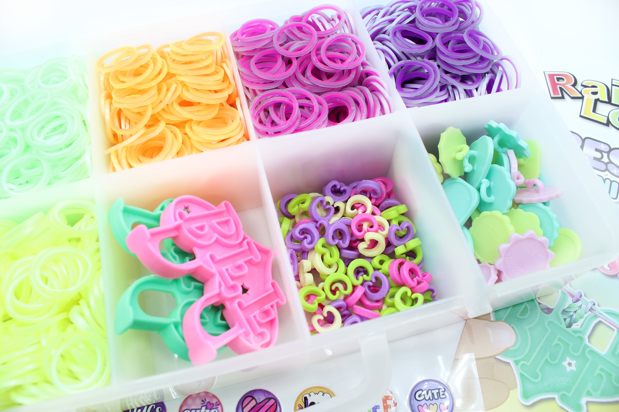 Colorful rubber band sets in compartments with a 'Rainbow Loom' box in the background.