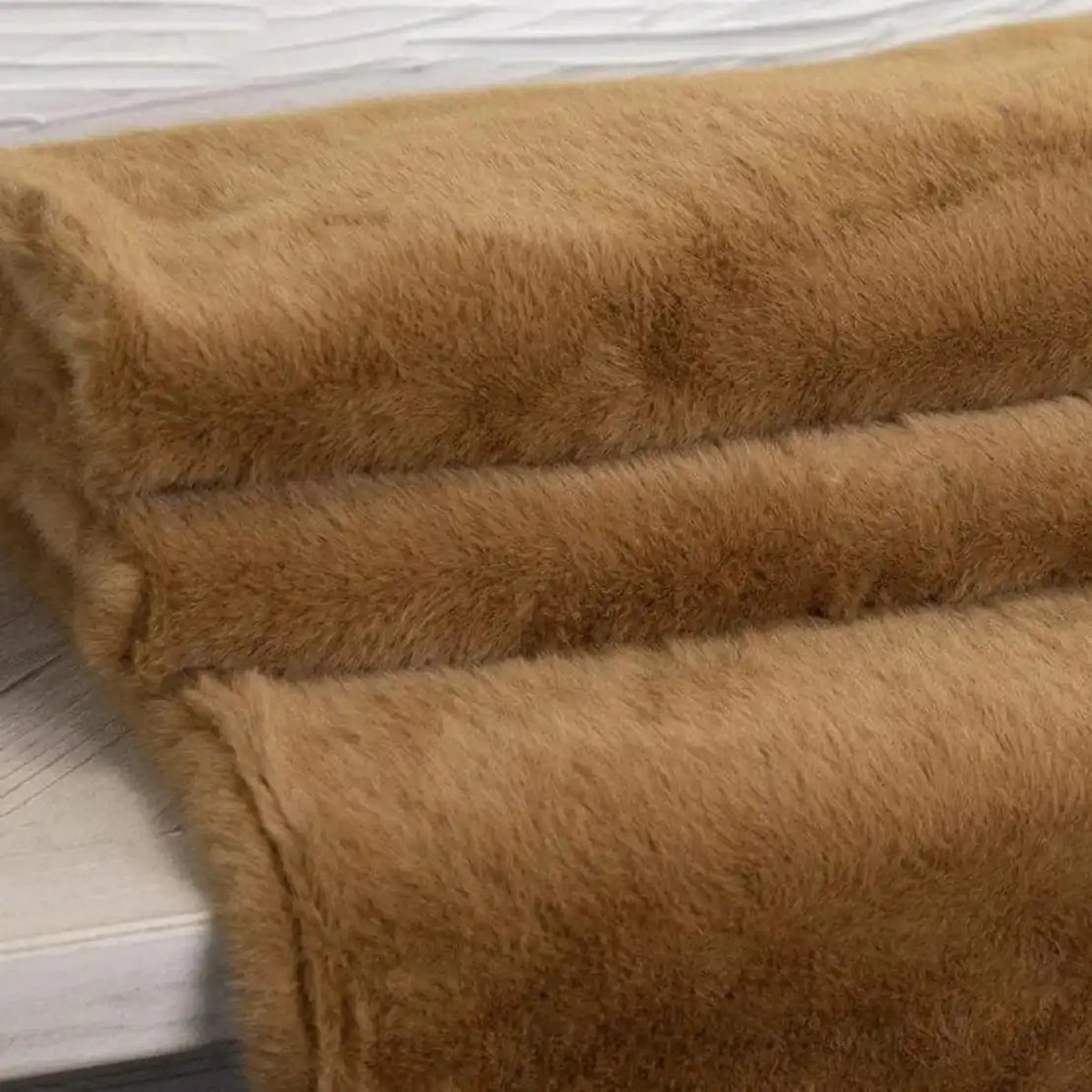 A close-up of a folded Ralph Throw in Cognac blanket or throw, showing its soft, plush texture against a light wood background.
