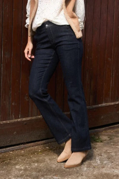 Person wearing dark blue jeans and a light-colored top against a wooden wall.