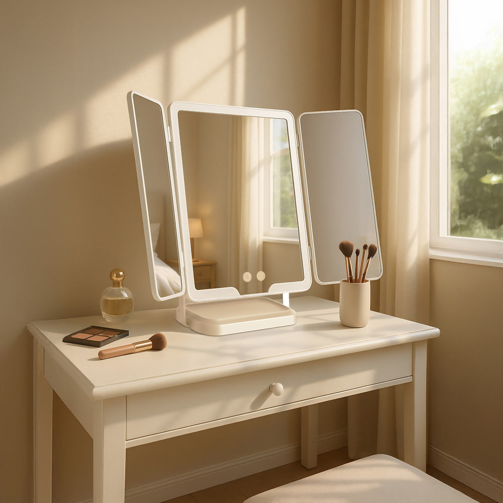 A Hollywood Rechargeable Portable Mirror with a three-sided folding mirror, styled with makeup brushes, a perfume bottle, and a compact in a warm, sunlit room.