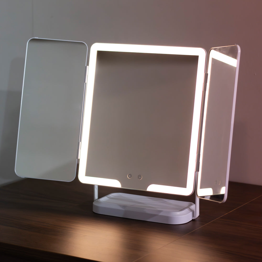 A tHollywood Rechargeable Portable Mirror with a white base, shown lit up on a dark wooden table against a neutral wall.