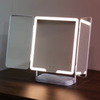 A tHollywood Rechargeable Portable Mirror with a white base, shown lit up on a dark wooden table against a neutral wall.