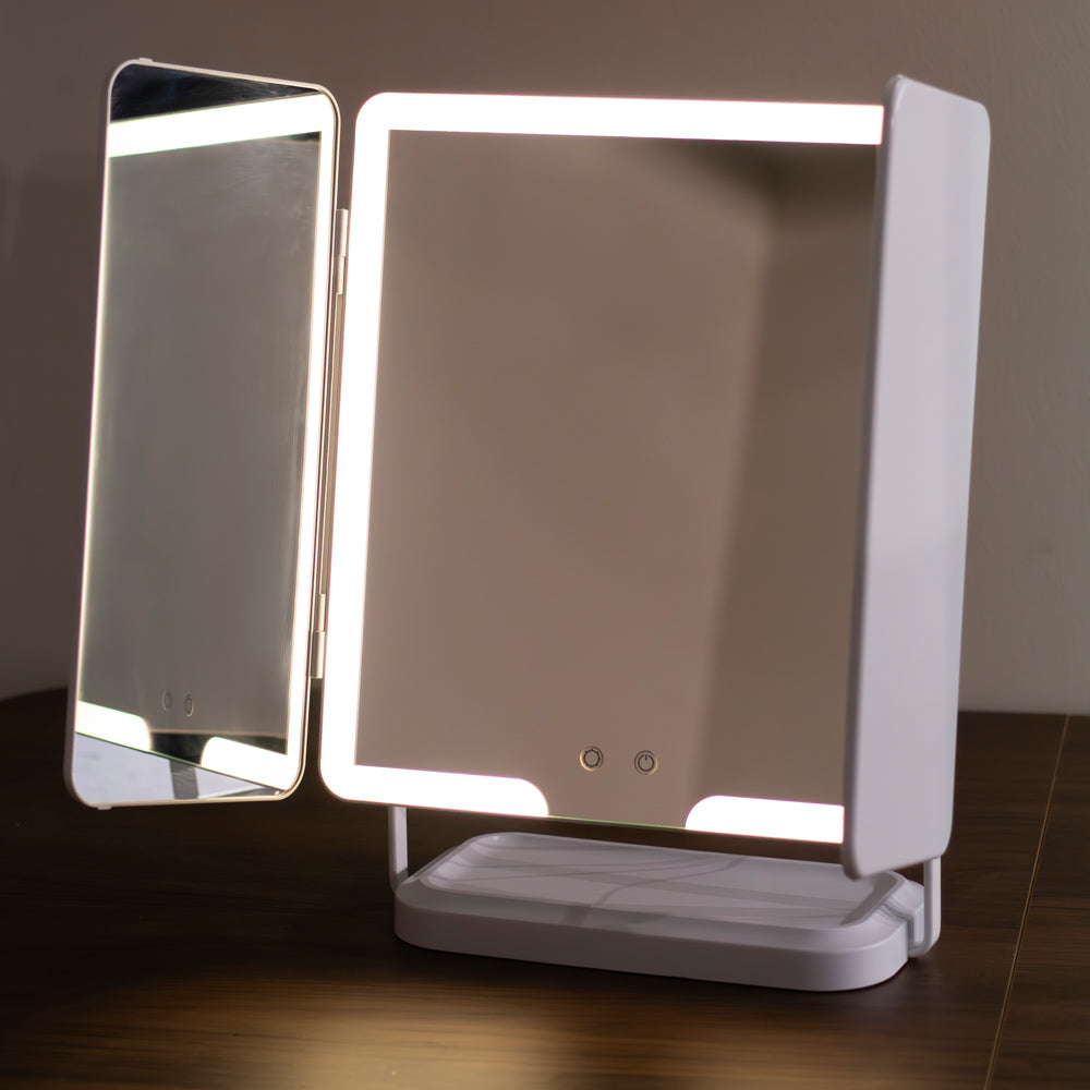 Hollywood Rechargeable Portable Mirror with a tri-fold design, shown open on a dark wooden table against a neutral wall. The main mirror is illuminated, and a smaller side mirror is swung out to the left.
