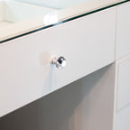 A close-up of a white wooden vanity drawer featuring a faceted clear crystal knob, with a glass top edge visible above.