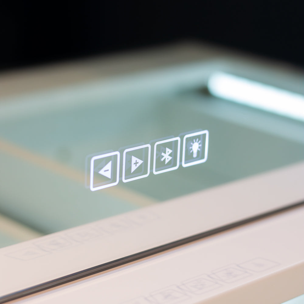 Close-up of a glossy light-activated control panel with four white media-style icons (rewind, play, Bluetooth, brightness) on a pale beige device against a dark background.