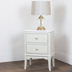 Monroe 2 Drawer Accent Table in Stone with two drawers and a lamp on a wooden floor against a white wall.