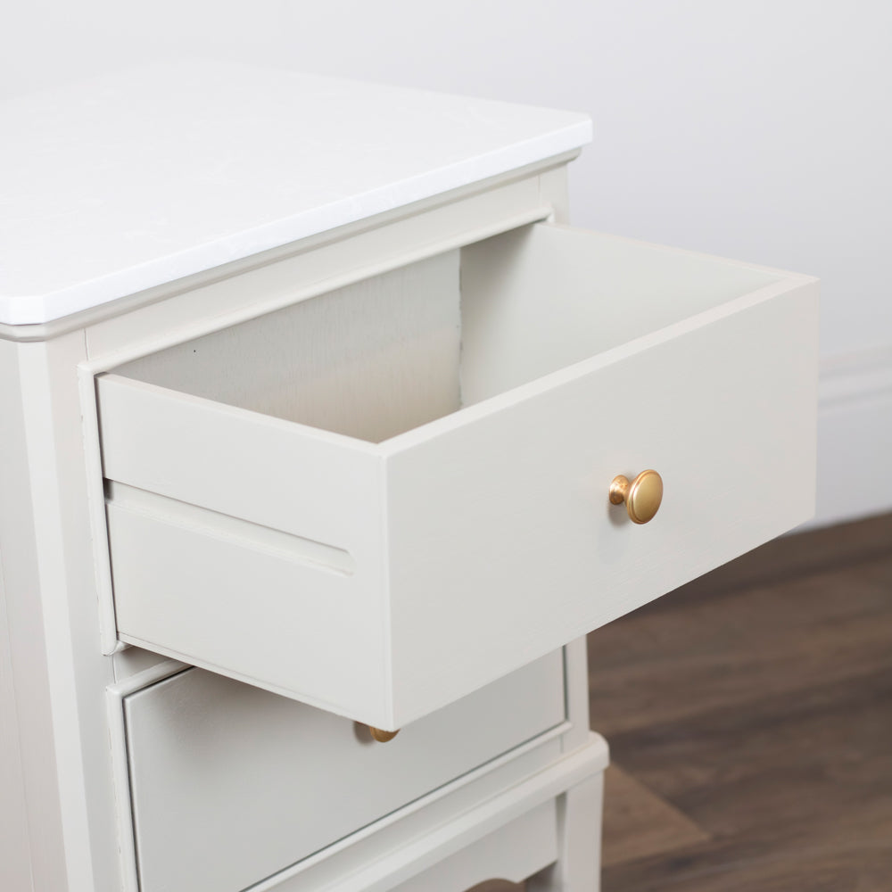 Monroe 2 Drawer Accent Table in Stonewith an open drawer showcasing a round gold pull knob, set against a light wall and dark wood floor.