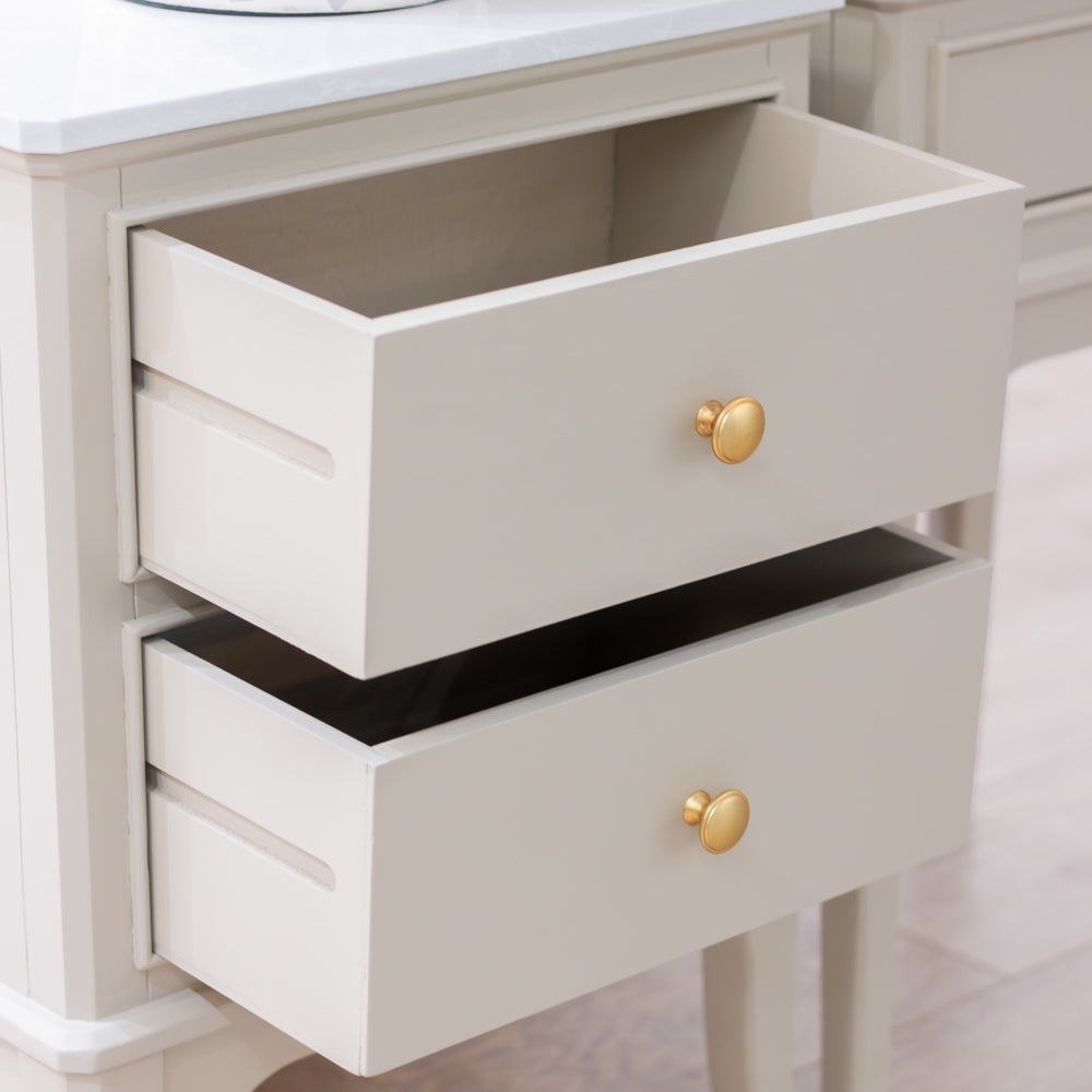 A close-up of a white two-drawer dresser with gold round knobs, showing the open top drawer and the bottom drawer partially open.