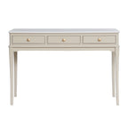 A console table with three drawers, featuring a light gray top and a warm beige body with gold-toned round knobs and slender legs.