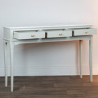 Monroe 3 Drawer Console Table in Stone with three drawers on a wooden floor against a white wall.