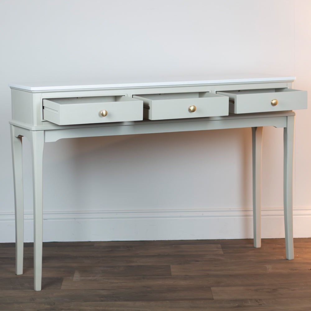 Monroe 3 Drawer Console Table in Stone with three drawers on a wooden floor against a white wall.