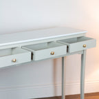 Monroe 3 Drawer Console Table in Stone console table with three drawers and brass knobs on a white wall background