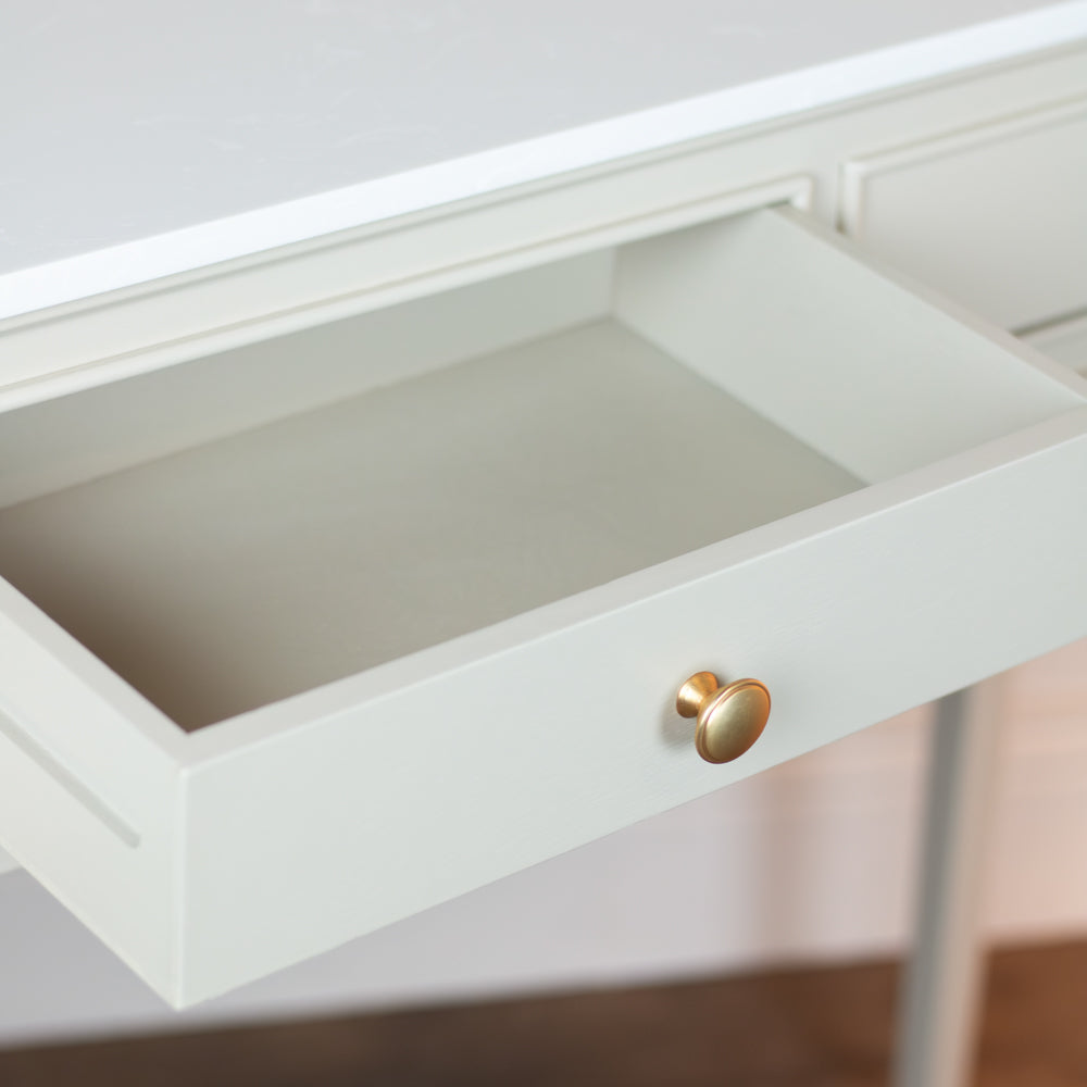 A close-up of a white drawer pulled open on a white desk, featuring a round gold metal knob.