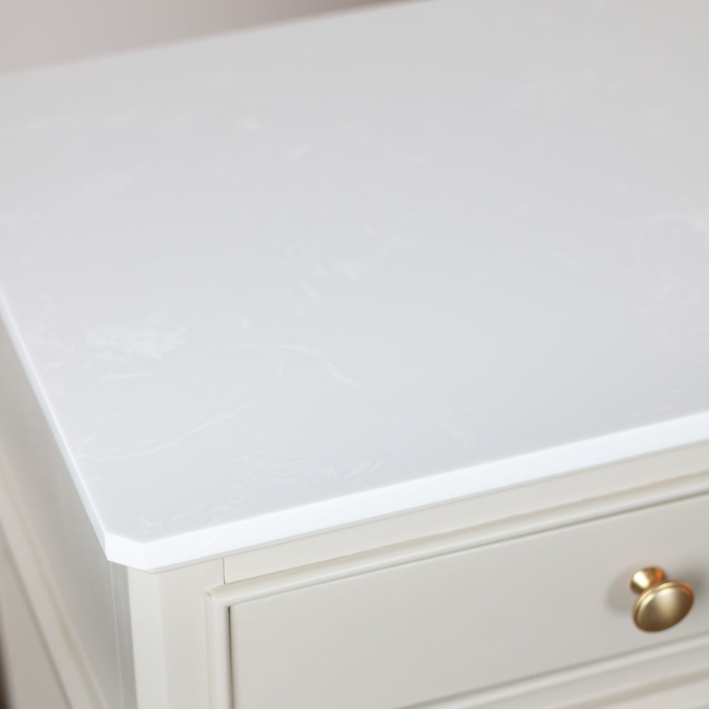 Close-up of a white tabletop or cabinet top with a subtle light floral pattern, shown above a drawer with a round gold knob.