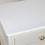 Close-up of a white tabletop or cabinet top with a subtle light floral pattern, shown above a drawer with a round gold knob.