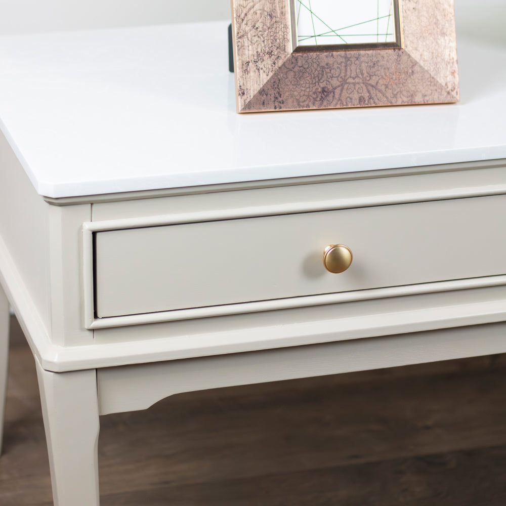 Monroe Coffee Table in Stone with a gold drawer handle on a wooden floor