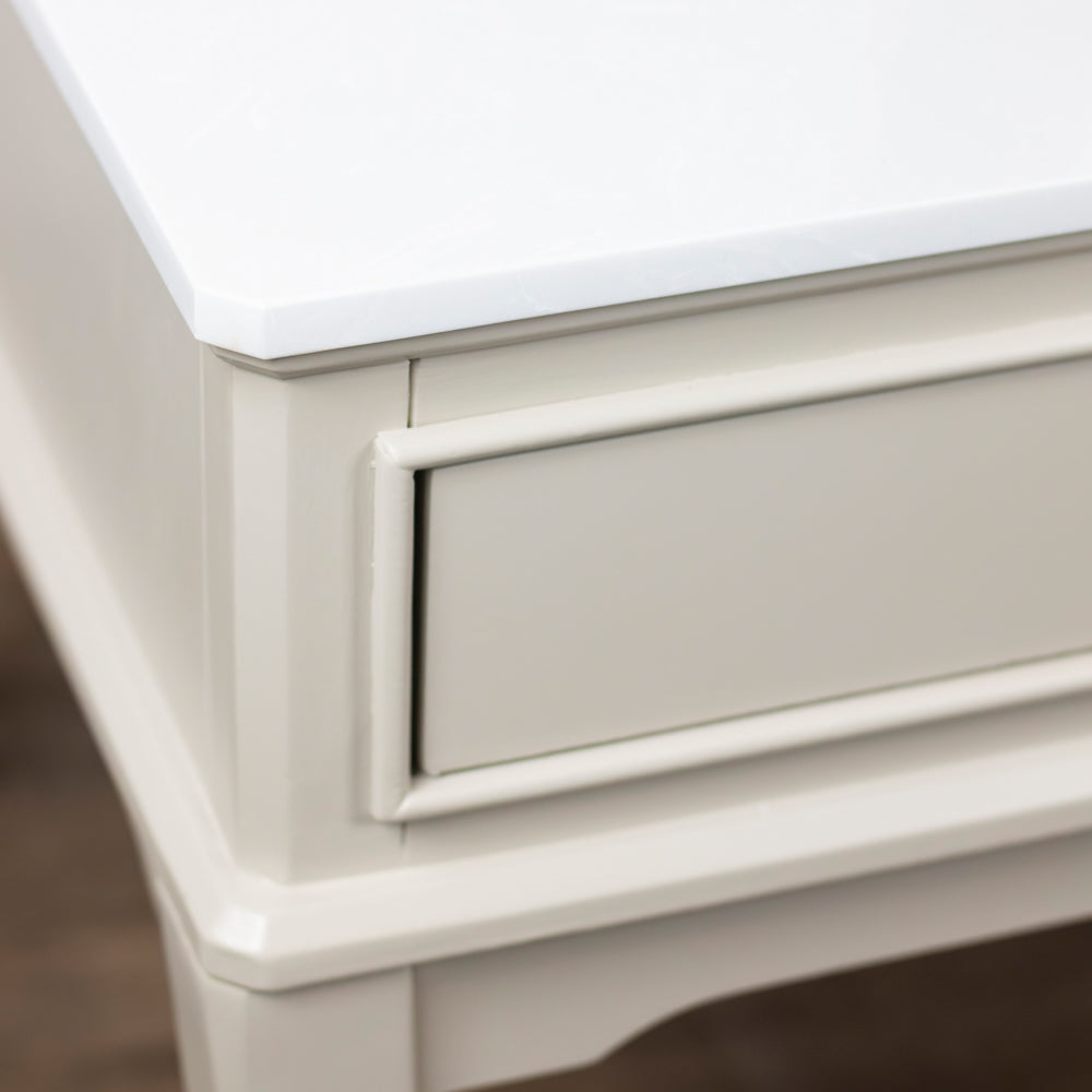 Close-up of a white wooden furniture piece, showing the corner of the top and a drawer front with decorative molding.