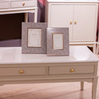 Two decorative picture frames with a textured gray and white patterned border, displayed on Monroe Coffee Table in Stone coffee  table in a living room setting.