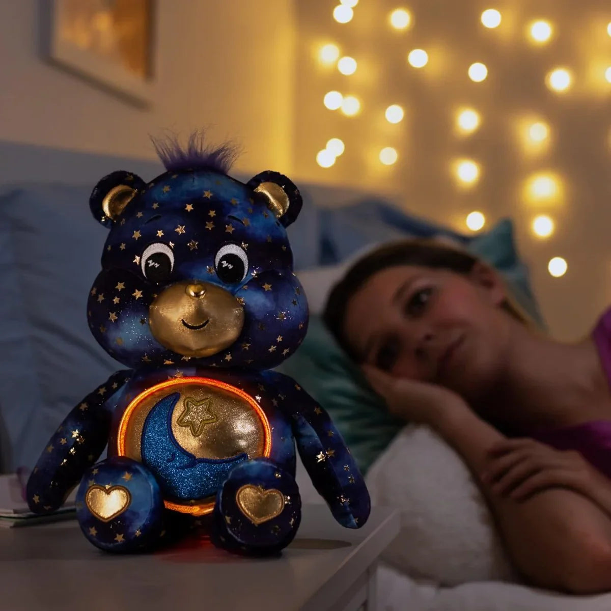 Decorative teddy bear with star patterns on a nightstand, illuminated by fairy lights in a cozy room.