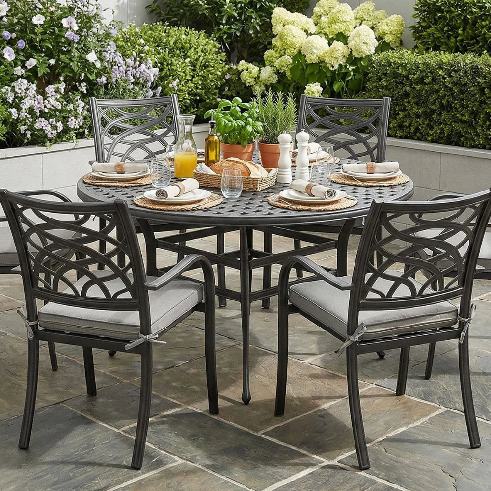 Outdoor patio set with table and chairs on a stone patio, surrounded by flowers and plants.
