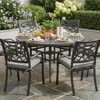 Outdoor patio set with table and chairs on a stone patio, surrounded by flowers and plants.