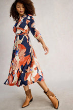 Woman wearing a colorful patterned dress with brown boots on a plain background