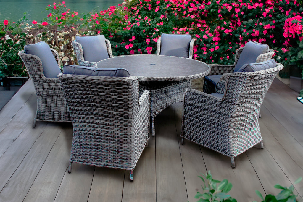 Outdoor patio set with a round table and six chairs on a wooden deck, surrounded by flowers.