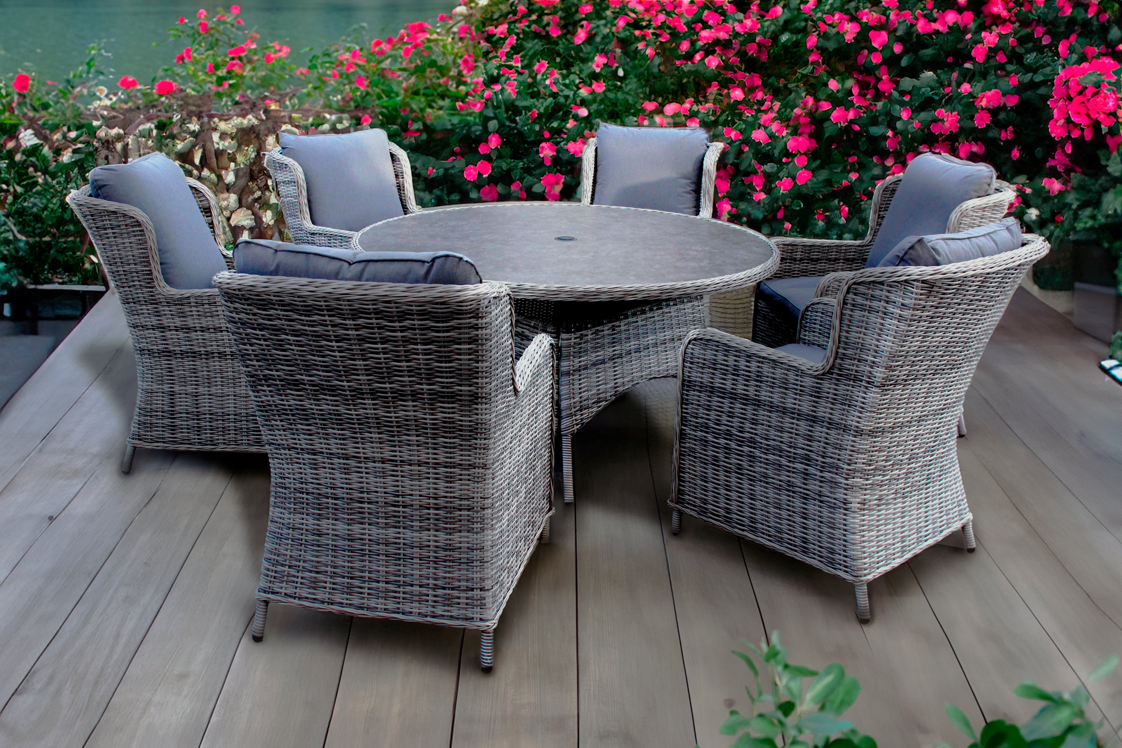 Outdoor patio set with a round table and six chairs on a wooden deck, surrounded by flowers.