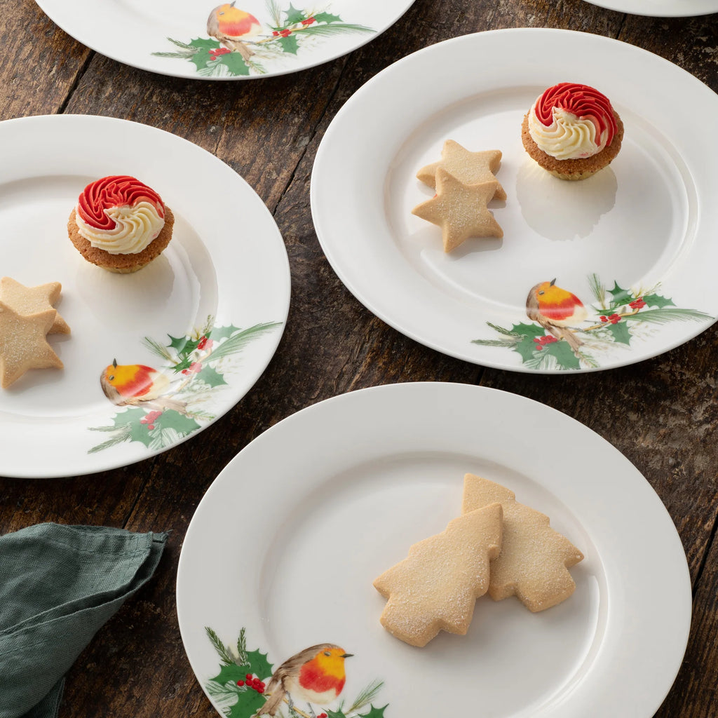 White plates with festive designs featuring cookies and small desserts on a wooden surface.