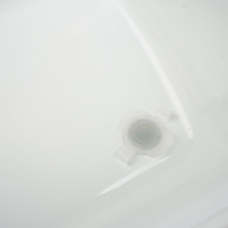 A close-up of a translucent white plastic cap or connector piece resting on a glossy white surface.