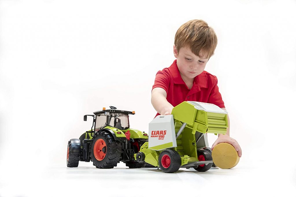 A Bruder Claas Round Baler toy, featuring a green and gray baler with a bale of hay attached, and red and black wheels and accents.