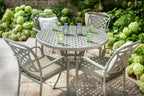 A 5-piece outdoor patio dining set featuring a round metal table and four matching chairs with cushioned seats, styled on a stone patio with green hydrangeas in the background.