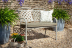 A white metal garden bench with two lattice-back seats and a cushioned seat and backrest, styled in a stone patio setting with potted plants and a decorative pillow.