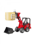 A toy model of a red Schaffer Compact Loader 2630 with a black bucket and gripper attachment handling a yellow bale.
