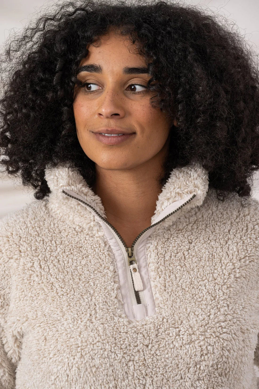 Woman wearing a beige fleece pullover with a neutral background