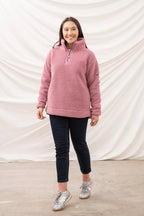 Woman wearing a pink pullover with a zipper, dark pants, and silver sneakers against a white backdrop.