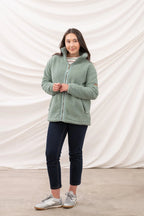 Woman wearing a green fleece jacket and dark pants against a white backdrop