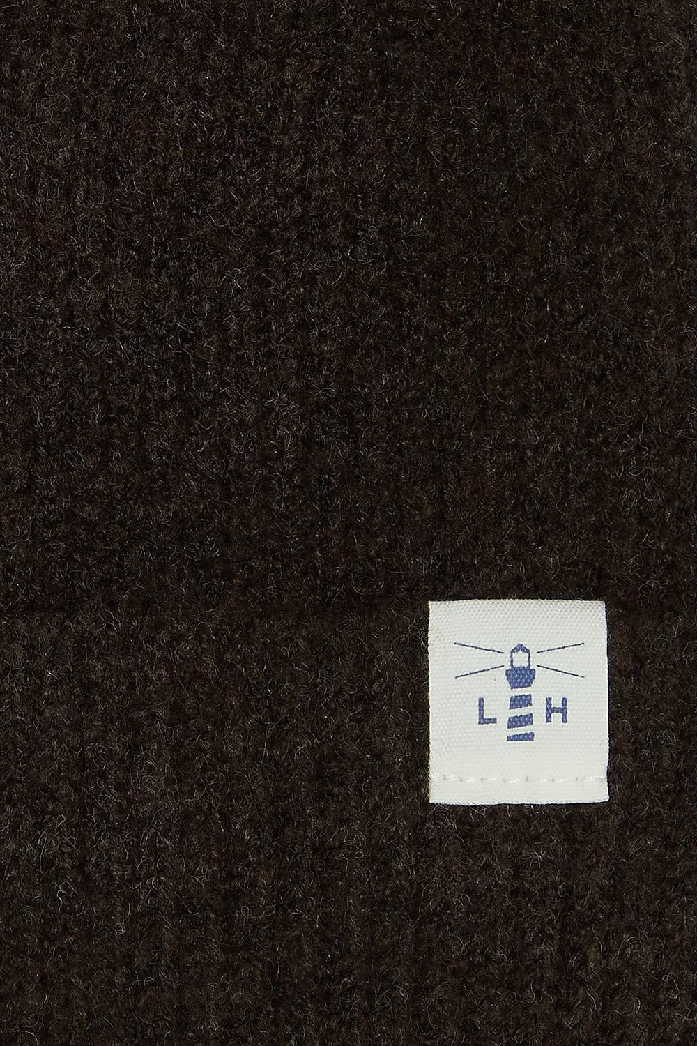 Close-up of a cocoa textured knit fabric with a small white square label featuring a blue lighthouse logo and the letters L.H.